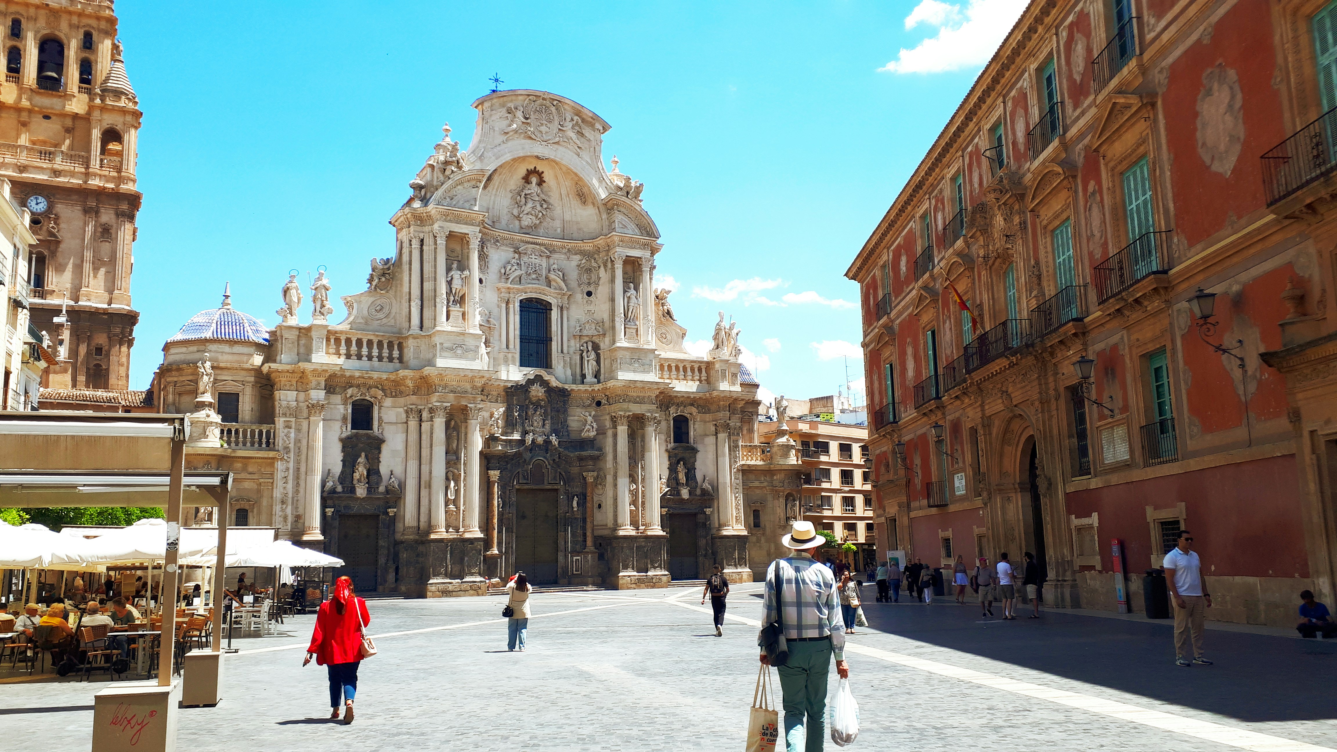 Plaza del Cardenal Belluga in Murcia, Spain, leading to the grand Murcia Cathedral, with sunlit historic buildings and people strolling across the square